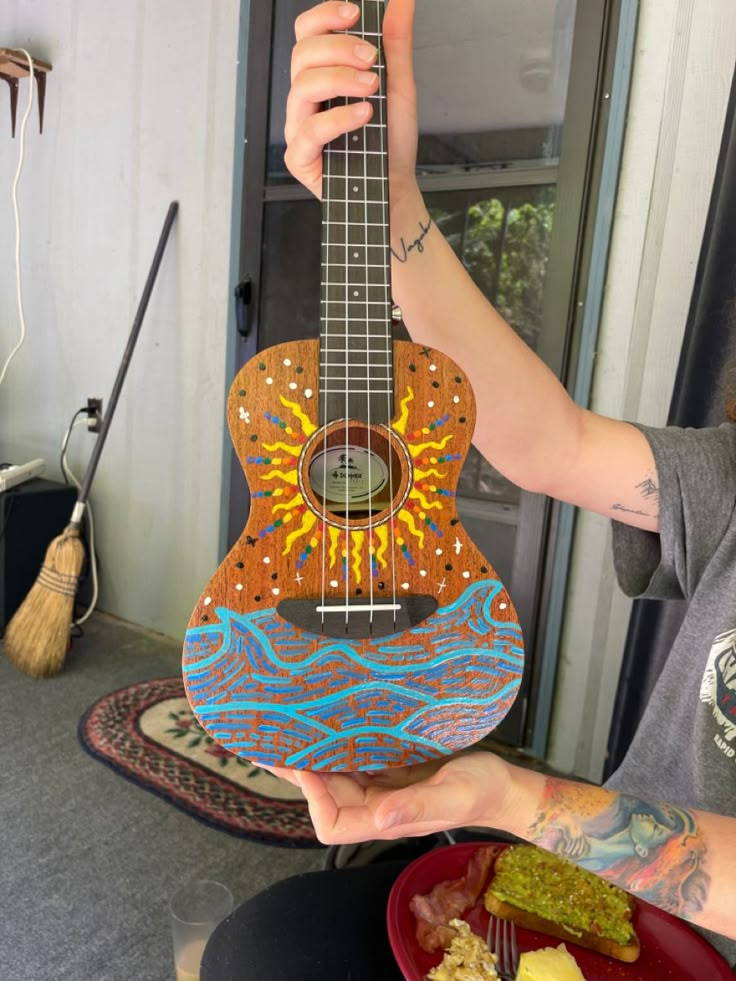 a woman holding up a colorful guitar in front of her face with food on the plate