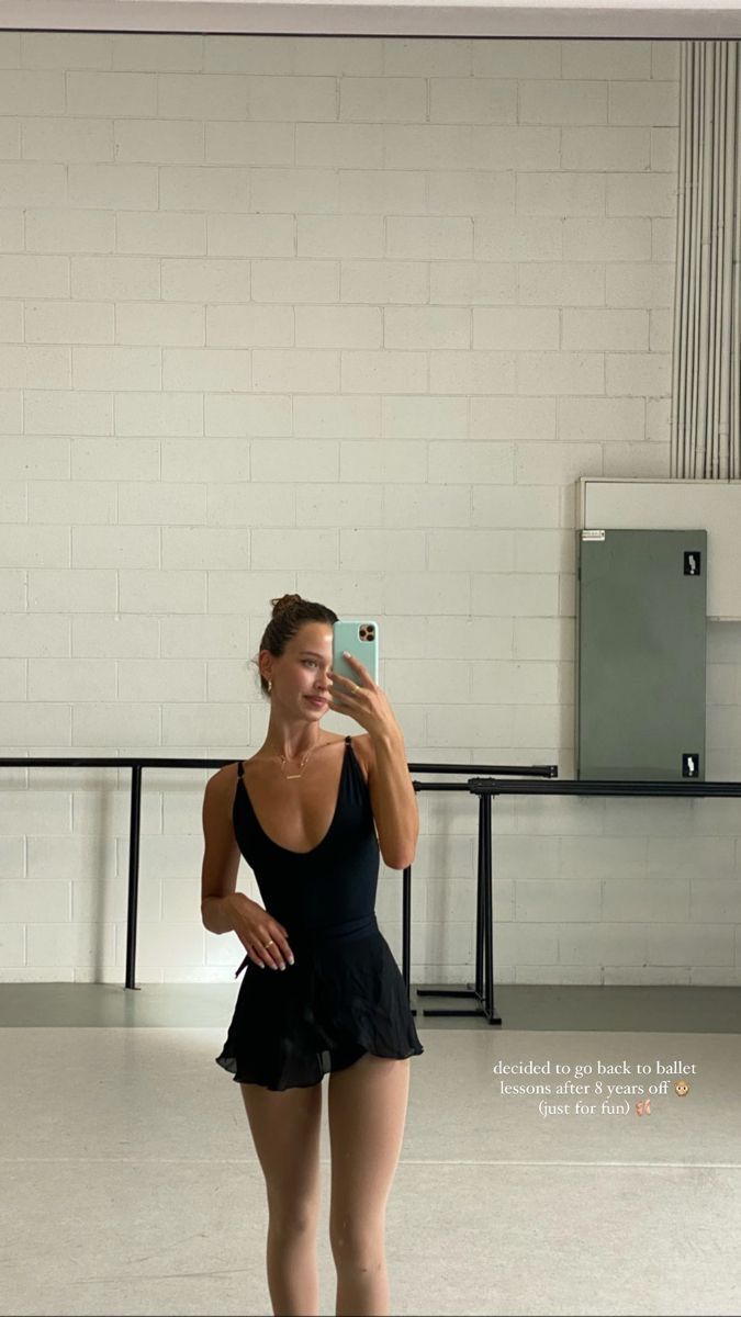 a woman taking a selfie with her cell phone in a dance studio while wearing a black leotard