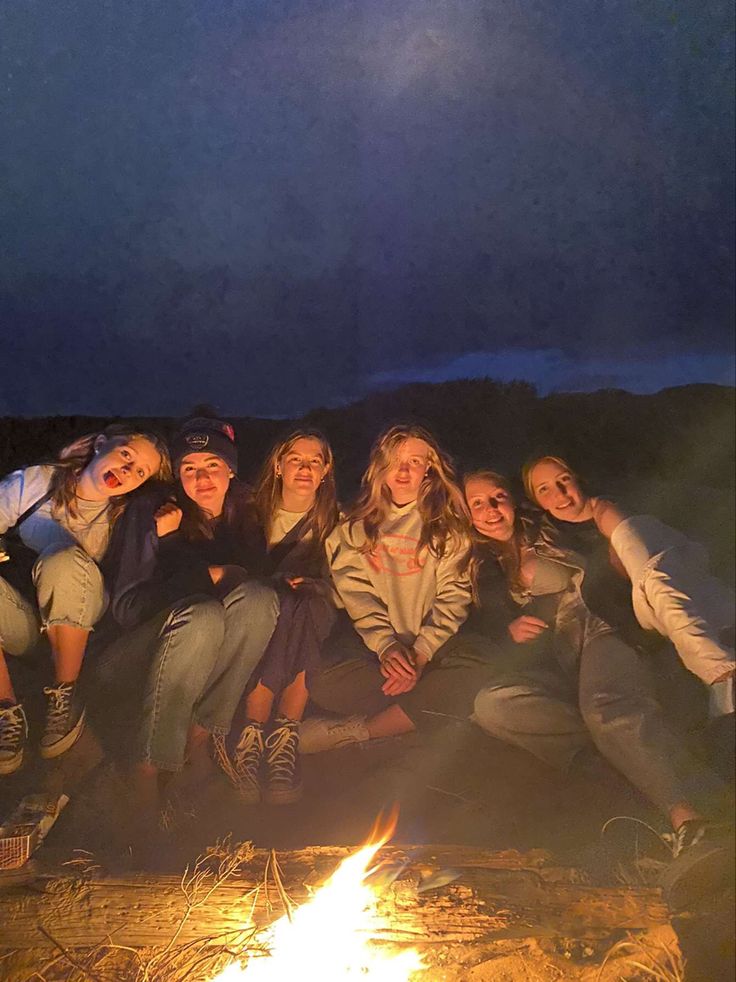 a group of young women sitting around a campfire with their arms around each other