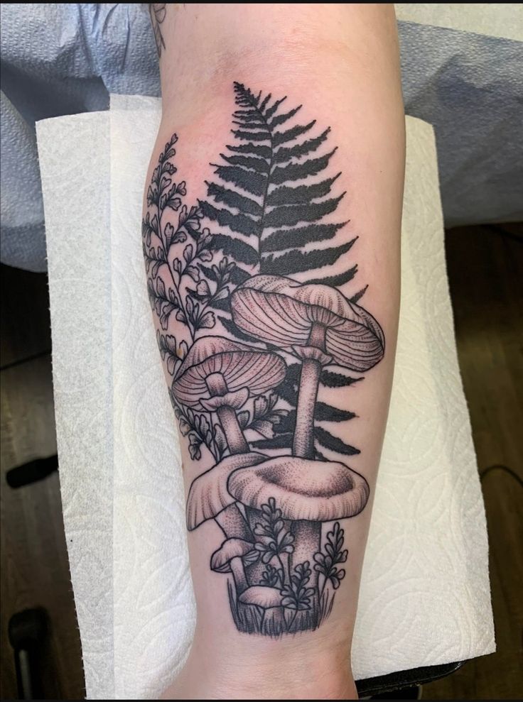 a black and white tattoo of mushrooms on the arm with ferns growing out of it