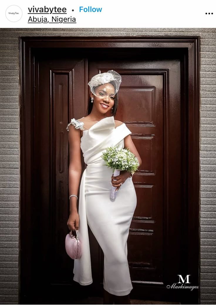 a woman wearing a white dress and holding a pink purse standing in front of a door