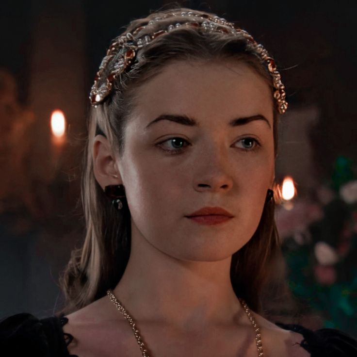 a woman wearing a tiara in a dark room with candles on the wall behind her