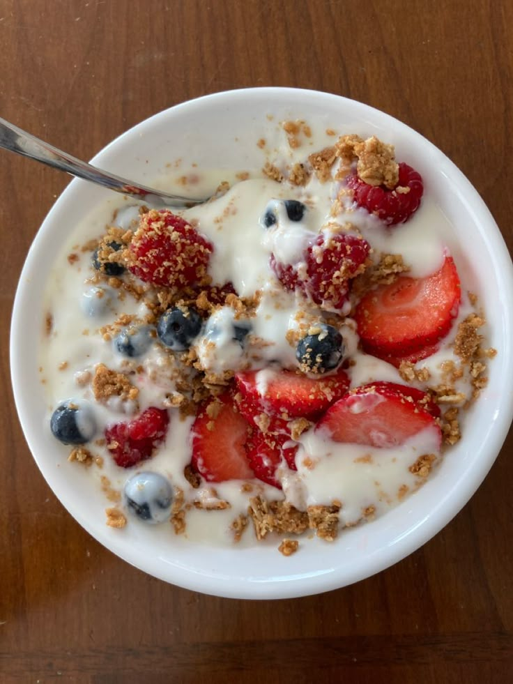 a bowl of yogurt with strawberries and blueberries in it on a wooden table