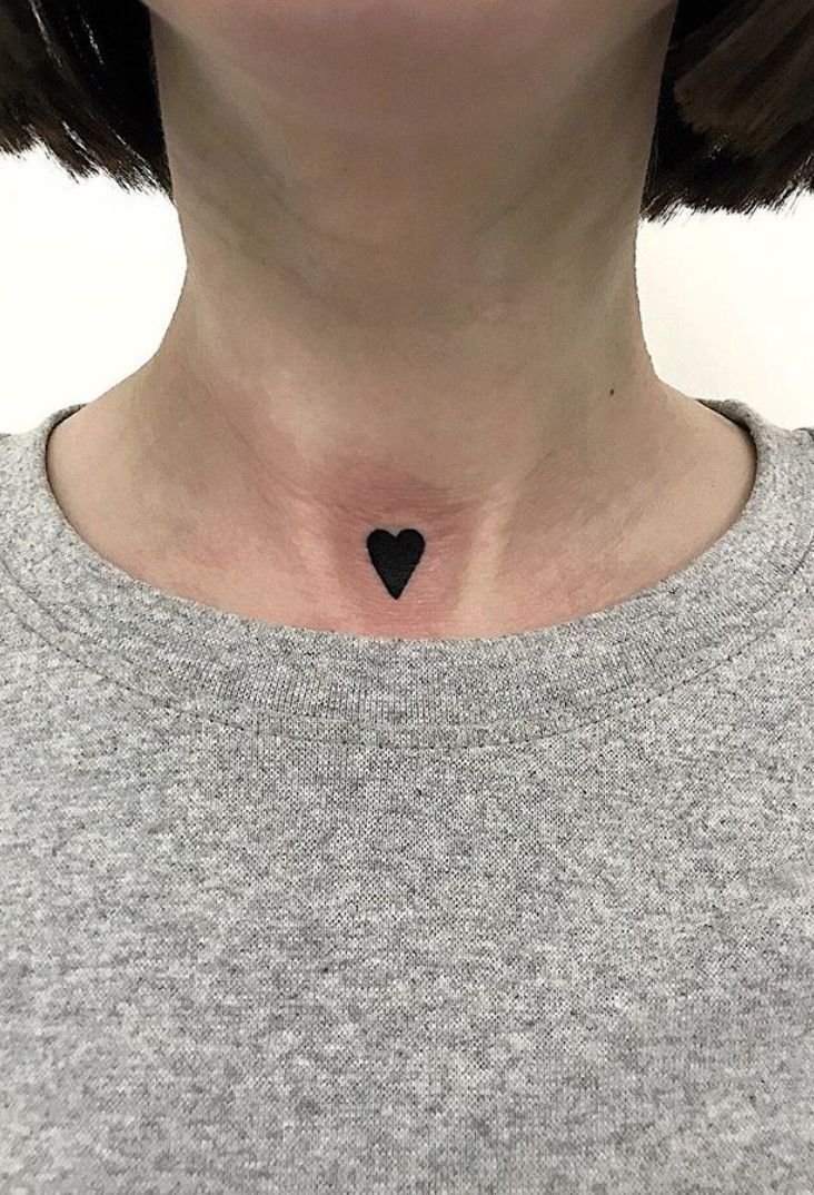 a woman's chest with a small heart tattoo on the side of her neck