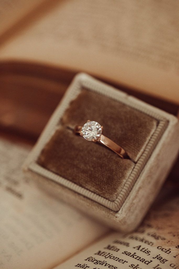 an engagement ring sits in a velvet box on top of an open book with pages