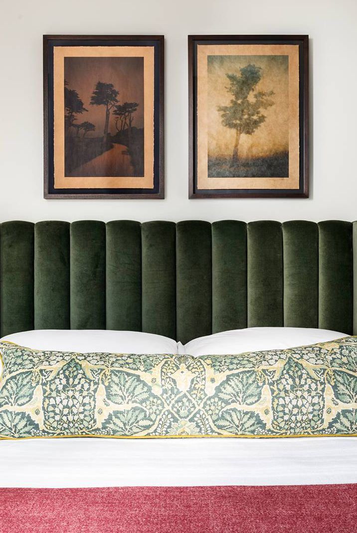 two framed pictures hang above a bed with green velvet headboard and pillows on it