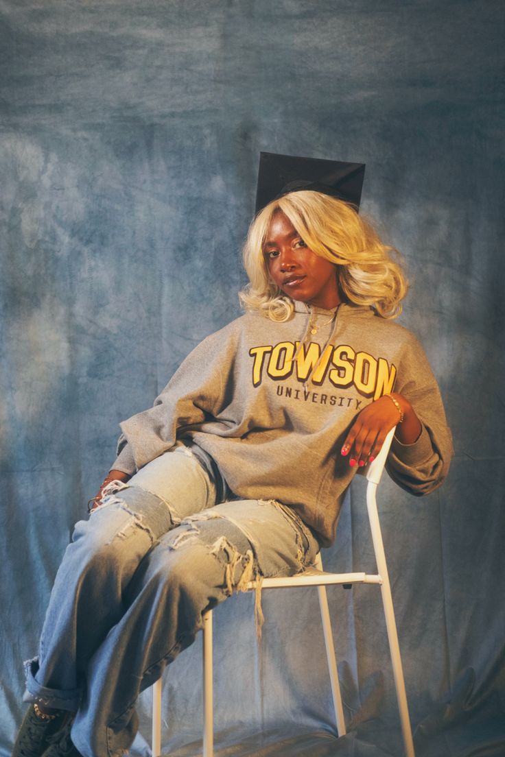 a woman sitting on top of a white chair wearing a graduation cap and grey sweatshirt