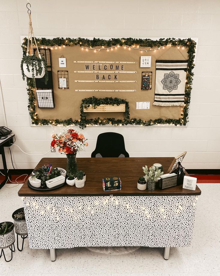 a table with flowers and potted plants on it in front of a welcome back sign