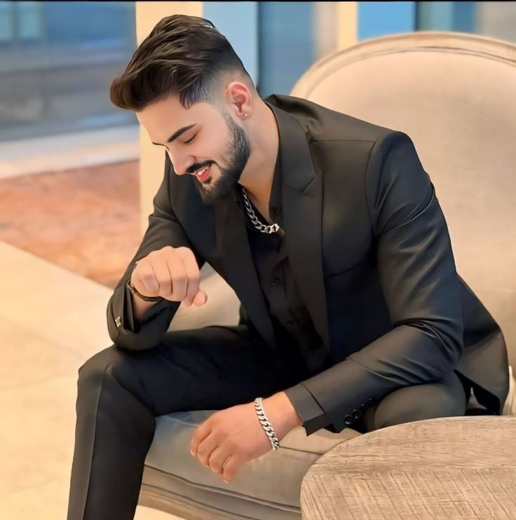 a man in a black suit sitting on a chair with his hand on his knee