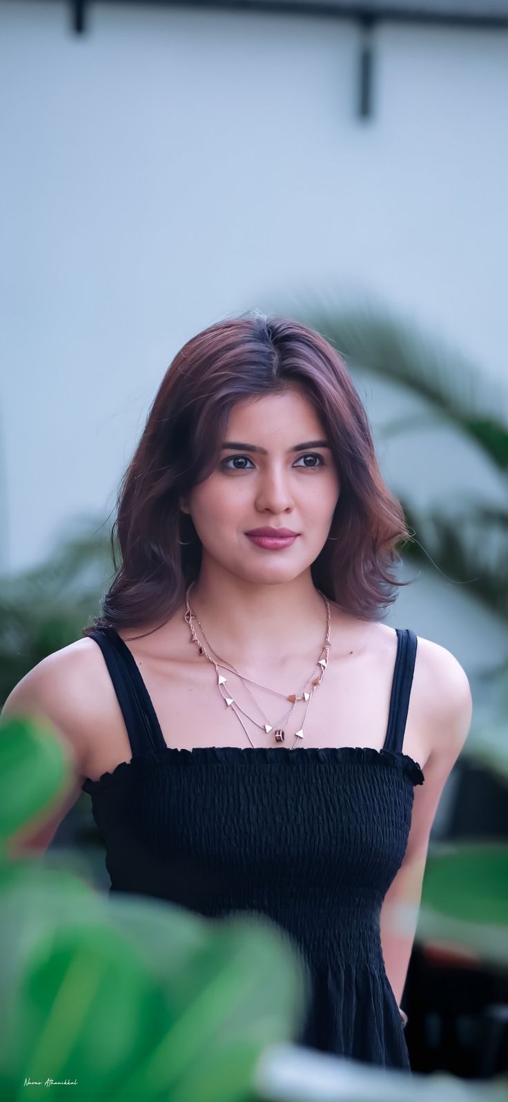 a young woman in a black dress posing for a photo with greenery behind her