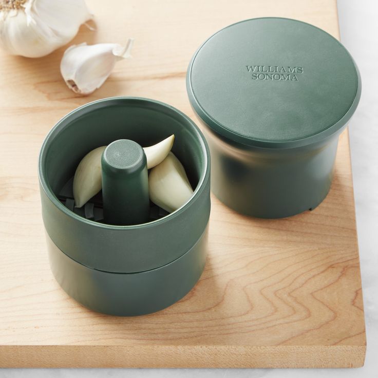 a couple of green containers sitting on top of a wooden cutting board next to garlic