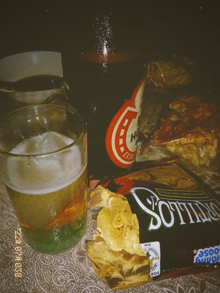 a glass of beer, chips and soda on a table