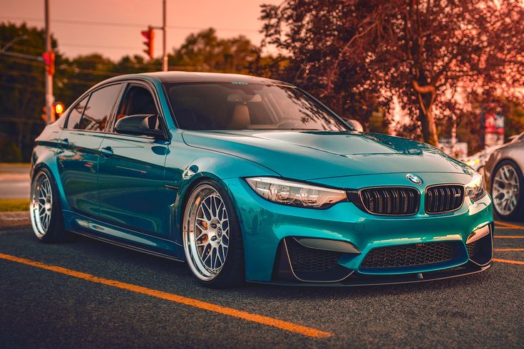 a blue bmw car parked in a parking lot next to another car on the street