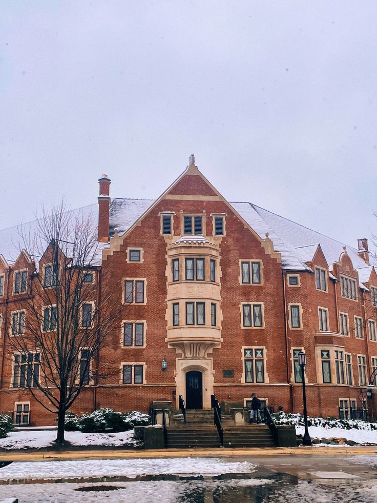 an old brick building with snow on the ground and steps leading to it, in front of some trees