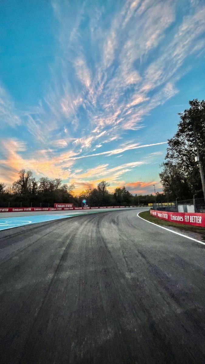 an empty race track with the sun setting in the distance and clouds above it, as seen from behind