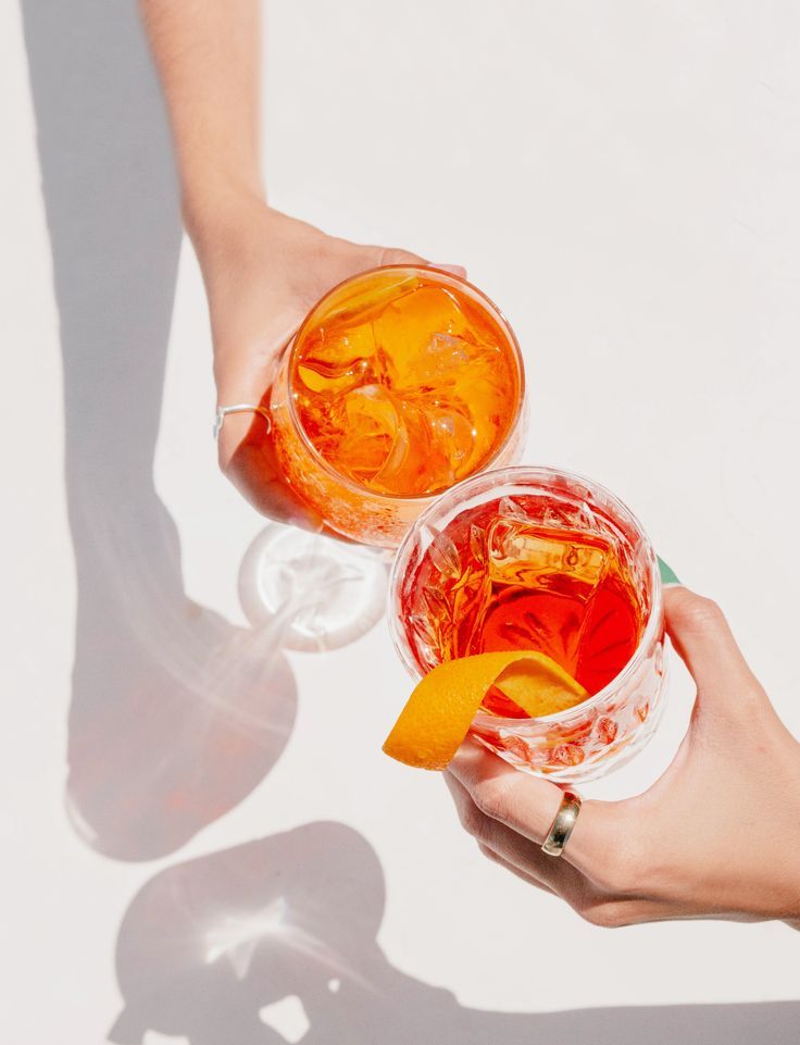 two people holding drinks in their hands with orange peels on the rim and one has an orange slice