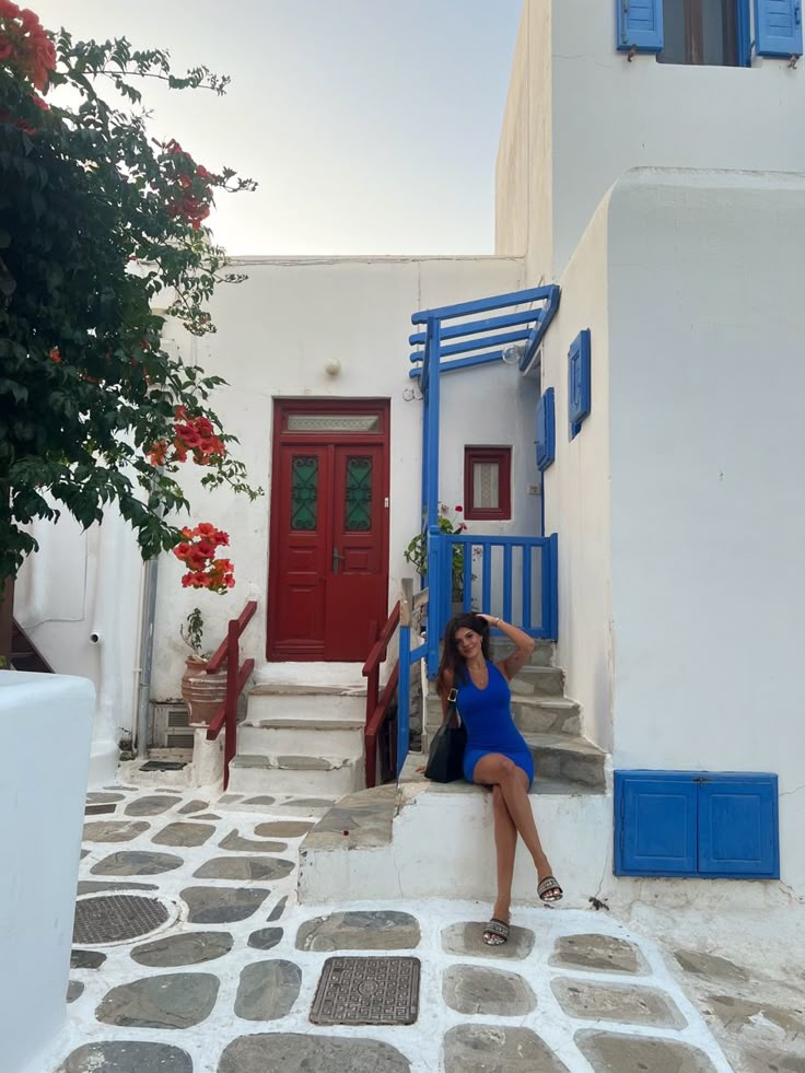 a woman sitting on steps in front of a building with blue shutters and red door