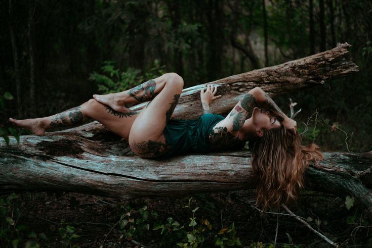 a beautiful woman laying on top of a fallen tree in the middle of a forest