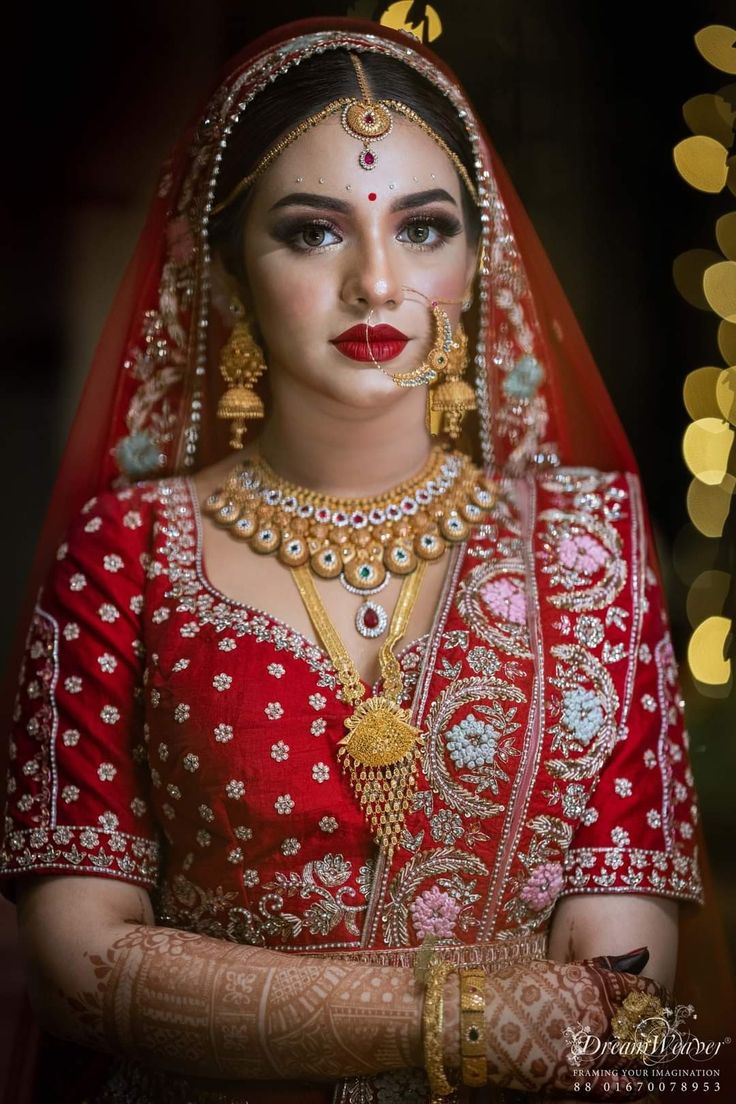 a woman wearing a red and gold bridal outfit with her hands on her chest