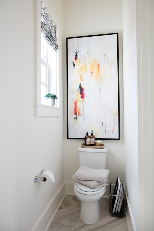 a white toilet sitting in a bathroom next to a window with a painting on the wall