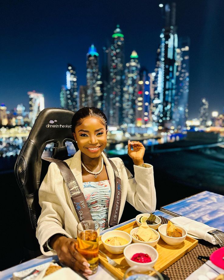 a woman sitting at a table with food and drinks in front of the city skyline