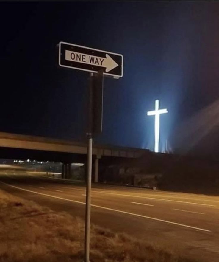 a one way street sign in front of a cross on the side of a road