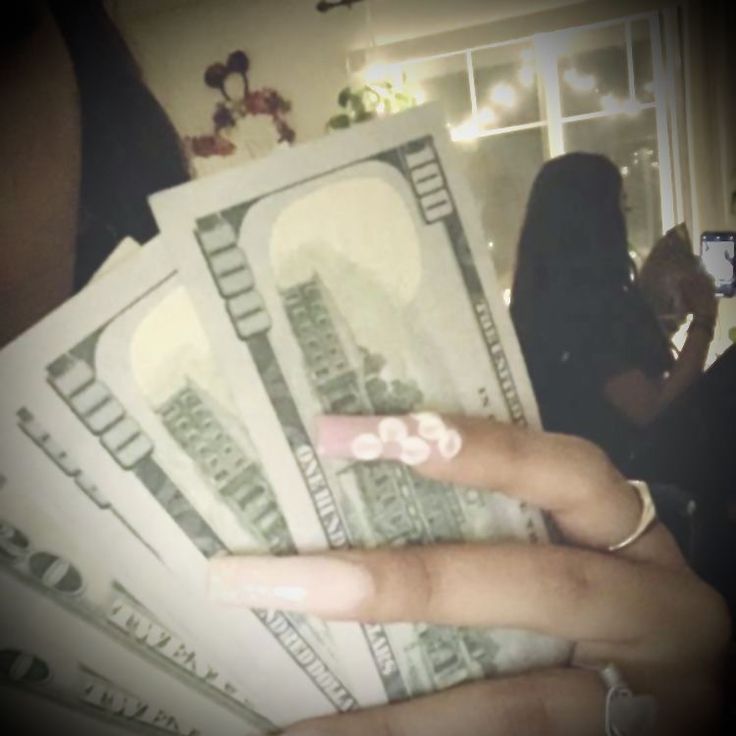 a woman's hand holding money in front of her face