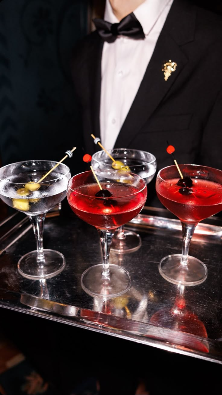 three martinis on a serving tray with olives and cherries in the glasses