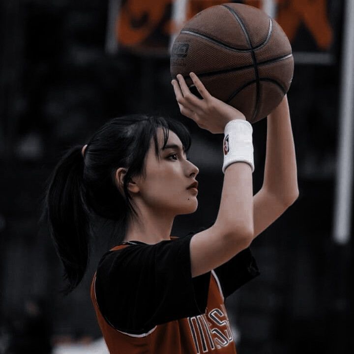 a woman holding a basketball up in the air with her right hand on top of it