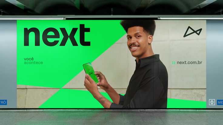 a man holding a smart phone in front of a green next advertisement on the wall