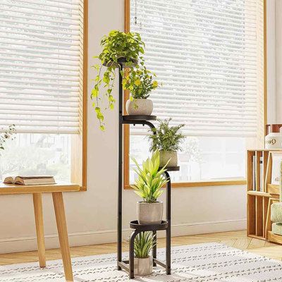 a living room filled with lots of plants next to a window covered in blind shades