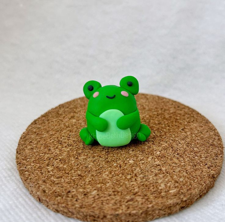 a green frog sitting on top of a cork coaster