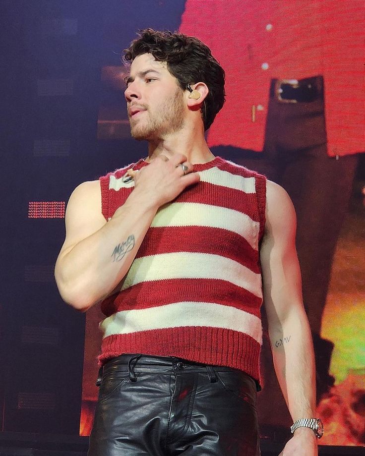 a man in leather pants and a striped shirt is standing up with his hand on his chest