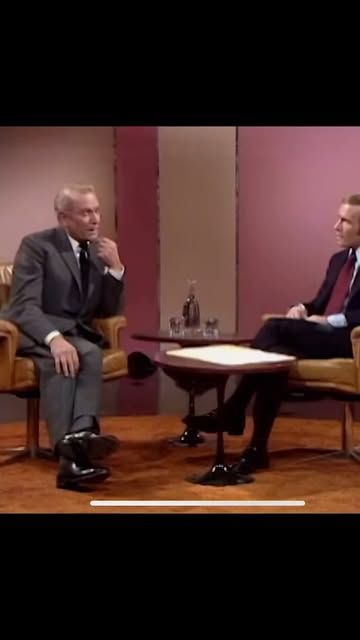 two men sitting in chairs talking to each other on the set of a television show