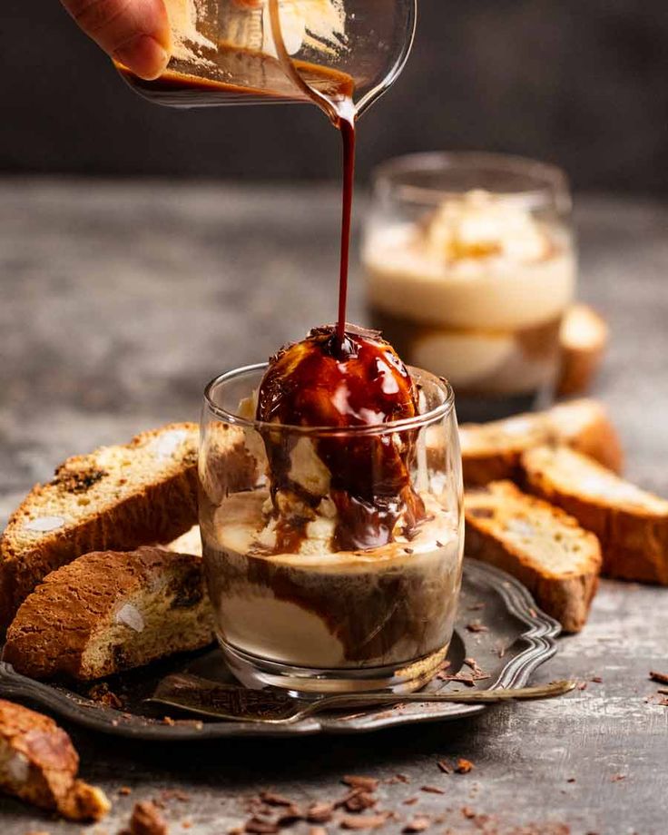 someone pouring ice cream into a dessert in a small glass dish with toasted bread on the side