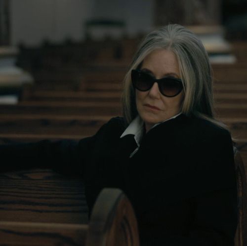 an older woman wearing sunglasses sitting on a bench in a church with her arms crossed