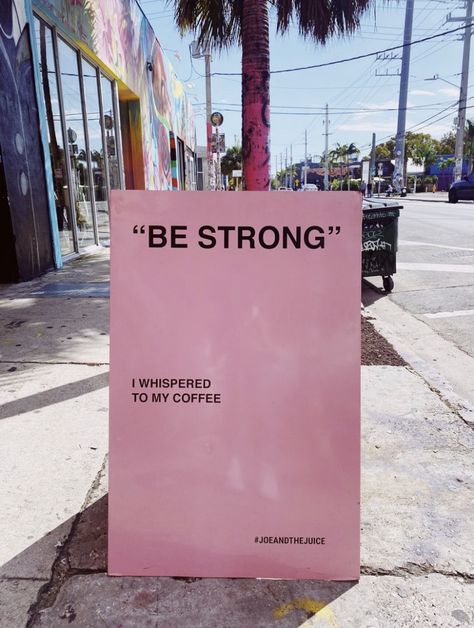 a pink sign sitting on the side of a road next to a palm tree in front of a store