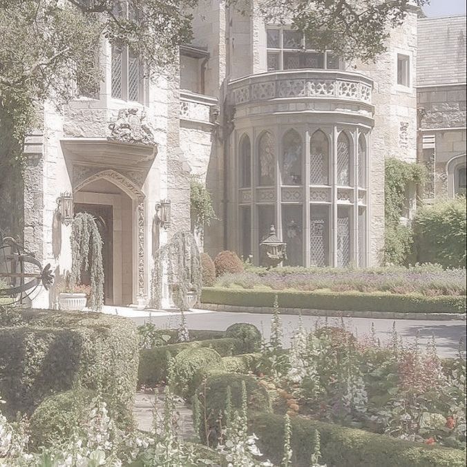 a large white house with lots of bushes and flowers in front of the entrance to it