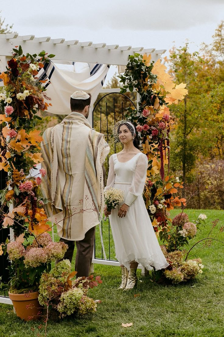 a bride and groom standing in front of an arch decorated with fall leaves for their wedding ceremony