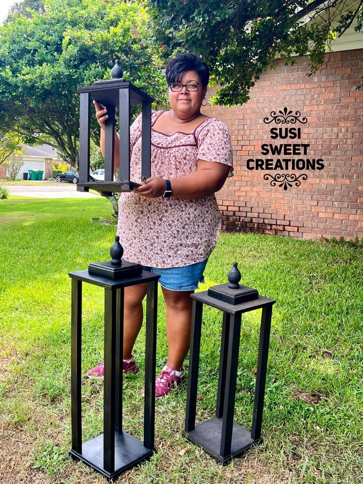 a woman standing next to two black metal lanterns in front of a brick building with the words susi sweet creations on it