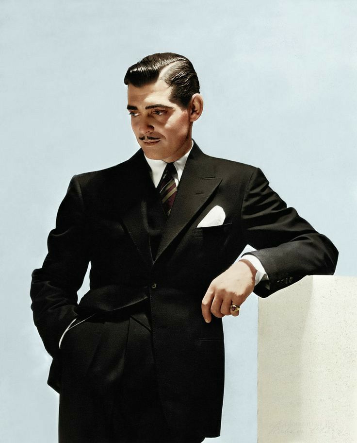 a man in a suit and tie leaning against a wall with his hands on his hips