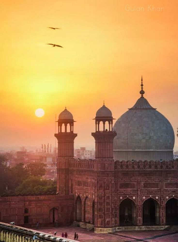 the sun is setting over an old building with two towers and birds flying in the sky