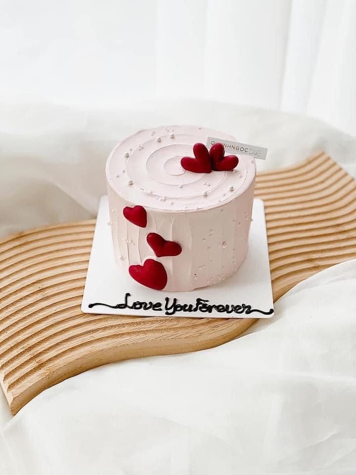 a white cake with red hearts on it sitting on a wooden tray next to a pillow