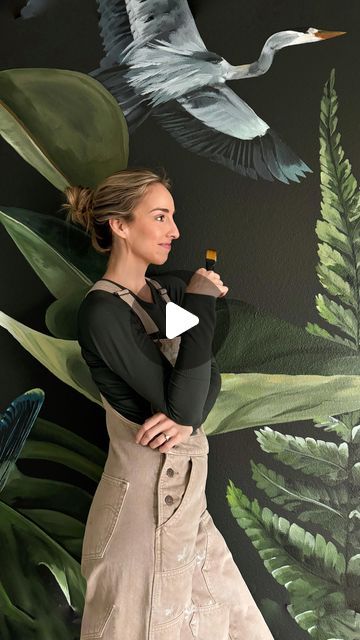 a woman standing in front of a wall painting with birds and plants on the walls