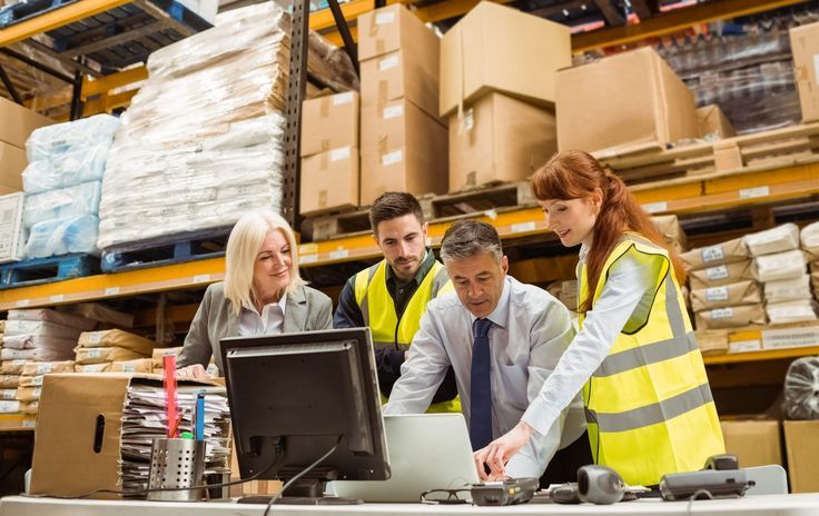 three people standing around a computer in a warehouse