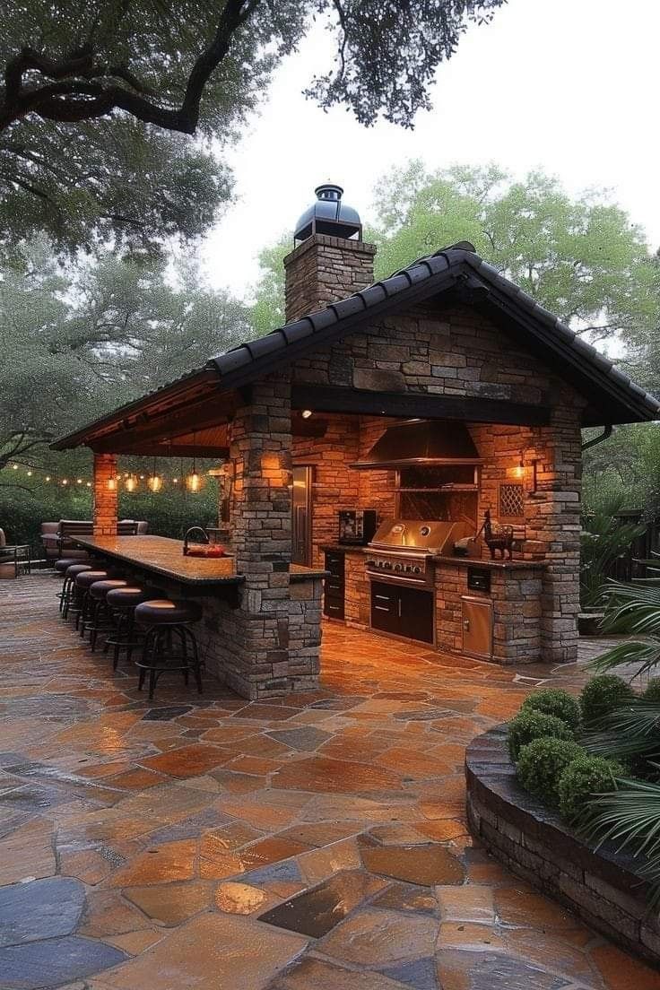 an outdoor kitchen is lit up at night with lights on the roof and grilling area