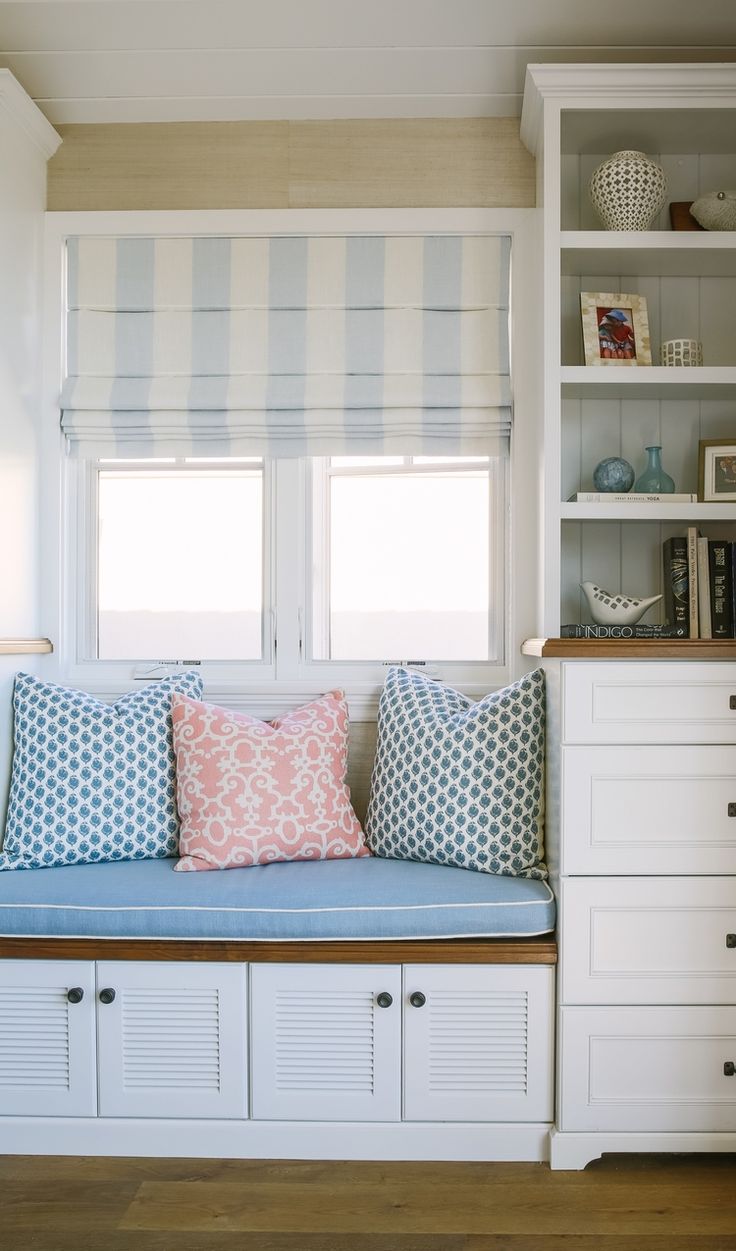 a window seat with pillows on it in front of a bookshelf and cabinets