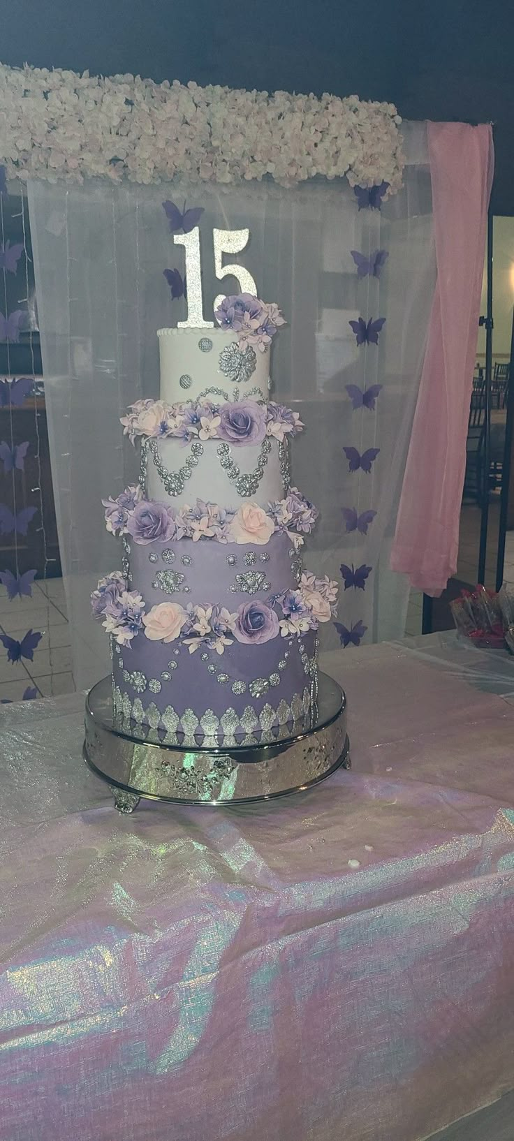 a purple and white wedding cake with butterflies on the top is sitting on a table