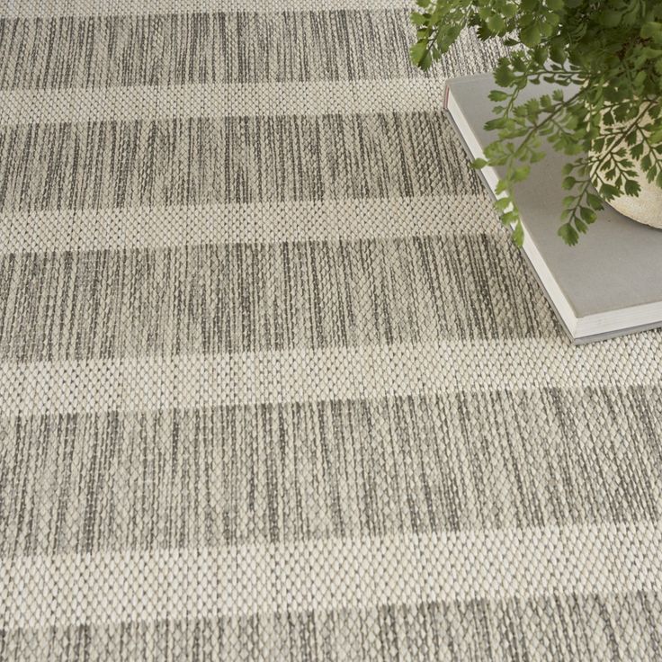 a plant is sitting on the floor next to a carpeted area with gray and white stripes