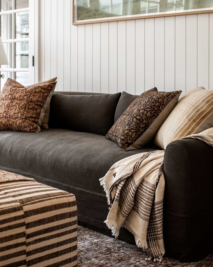 a living room with a couch, ottoman and pillows on top of the couch in front of a window